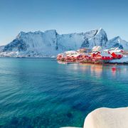 Rote Häuser am Ufer des Norwegischen Meeres. Sonnige Winteransicht des Fischerdorfes Sakrisoy
