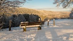 Mit Schnee bedeckte Holzbank in der Eifellandschaft im Winter
